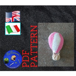 Può includere: Una mongolfiera all'uncinetto a righe rosa e bianche con un cestino beige. L'immagine include il testo "PDF PATTERN" in rosso, insieme alle bandiere di USA, Regno Unito e Italia e un logo.