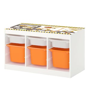 Puede incluir: Unidad de almacenamiento de juguetes blanca con tres compartimentos. Cada compartimento tiene un estante blanco y una papelera naranja. La parte superior de la unidad tiene un diseño de temática de construcción con rayas amarillas y negras.