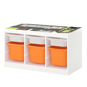 May include: White toy storage unit with three compartments. Each compartment has a white shelf and an orange bin. The top of the unit has a black and white playmat with a road design.