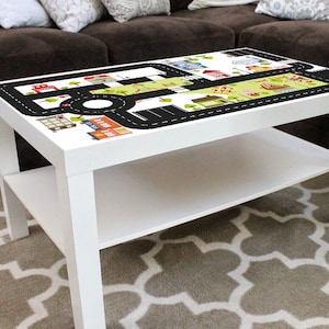 May include: White coffee table with a removable top featuring a black and white city road map design. The table has a lower shelf.
