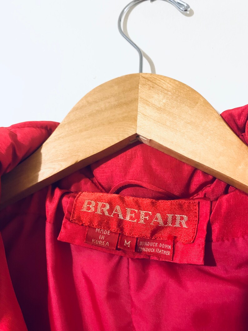 May include: Red down jacket with a label that reads "Braefair" and "Made in Korea". The label also indicates the jacket is size M and is made with 80% duck down and 20% duck feather.