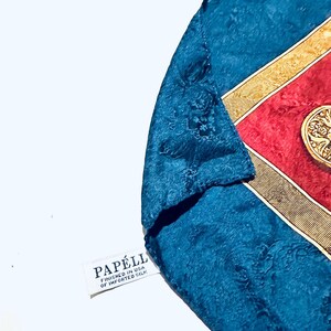 Puede incluir: Un pa&ntilde;uelo de seda azul con un borde estampado en oro y rojo. El pa&ntilde;uelo tiene una etiqueta blanca que dice "Papell, Finished in USA of Imported Silk".
