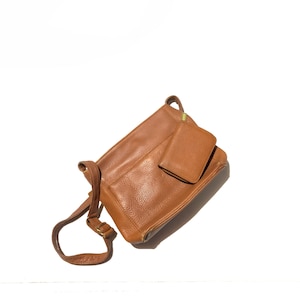 Puede incluir: Un bolso de hombro de cuero marrón con un bolsillo más pequeño en la parte delantera. El bolso tiene una correa larga ajustable.