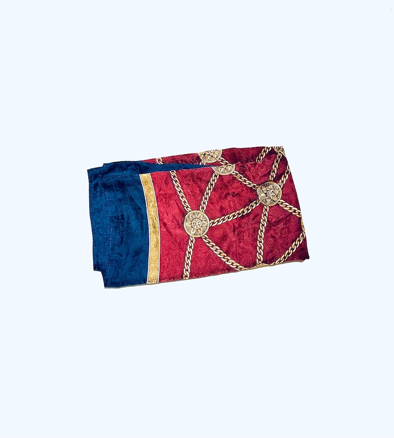Puede incluir: Una bufanda de patr&oacute;n rojo y azul con cadenas doradas y dise&ntilde;os circulares.