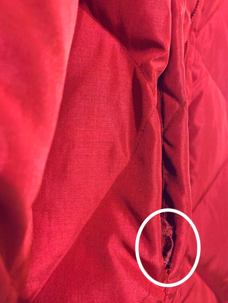 May include: A close-up of a red quilted jacket with a small tear in the seam. The tear is circled in white.