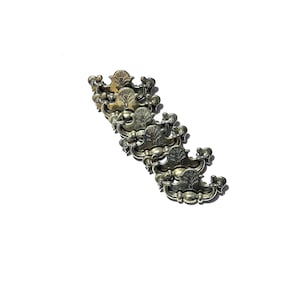 May include: A collection of antique silver-toned drawer pulls. Each pull features an ornate design with a central tree motif and decorative flourishes. The pulls are arranged diagonally against a white background.