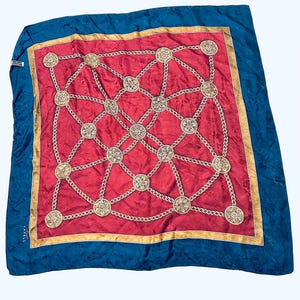 Puede incluir: Un pa&ntilde;uelo de seda rojo y azul con un patr&oacute;n de cadena dorada y medallones. El pa&ntilde;uelo tiene un borde dorado y el texto "PARELL" es visible en la esquina inferior izquierda.