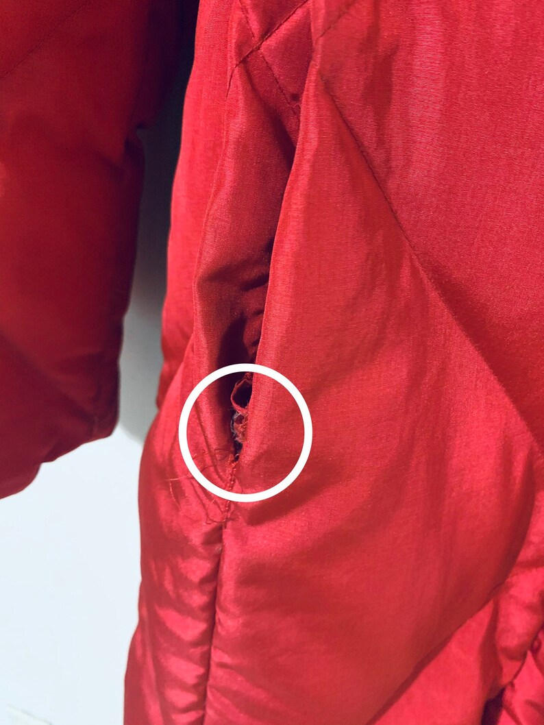 May include: A close-up of a red quilted jacket with a small tear in the fabric near the pocket.