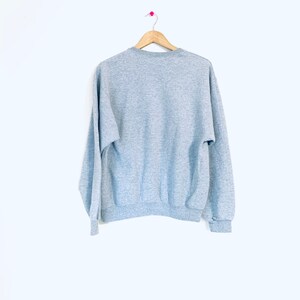 Puede incluir: Una sudadera gris jaspeada con mangas largas y cuello redondo.