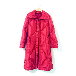 May include: A long, red puffer coat with a diamond quilted pattern. The coat has a high collar and a zipper closure.