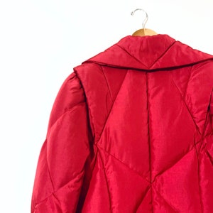 May include: A red quilted puffer jacket with a large collar, hanging on a wooden hanger.