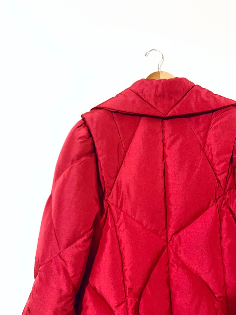 May include: A red quilted puffer jacket with a large collar, hanging on a wooden hanger.