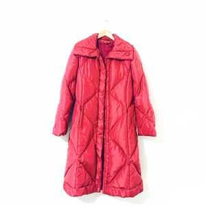 May include: A long, red quilted puffer coat with a stand-up collar and a zipper closure.
