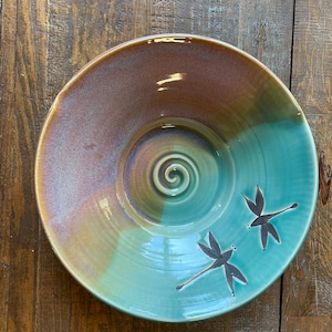 May include: A large, ceramic serving bowl with a teal glaze and a brown swirl design. Two dragonfly silhouettes are painted on the bowl.