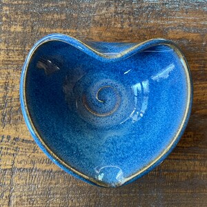 May include: A blue ceramic heart-shaped dish with a swirl design. The dish has a glazed finish and a brown rim.