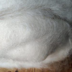 Puede incluir: Primer plano de una masa de fibras blancas y suaves. La textura es esponjosa y similar a una nube, con sutiles variaciones de luz y sombra. Las fibras están densamente empaquetadas, creando una apariencia voluminosa. El material es probablemente para manualidades o textiles.