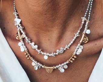 May include: A layered necklace with silver and gold beads and charms. The necklace features a variety of shapes, including hearts, circles, and triangles.