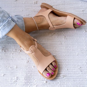 May include: A pair of light brown leather sandals with a t-strap design. The sandals have a simple, minimalist style and are perfect for warm weather.