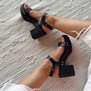 May include: Black platform sandals with a chunky heel and silver studs. The sandals have a strap across the toe and an ankle strap.