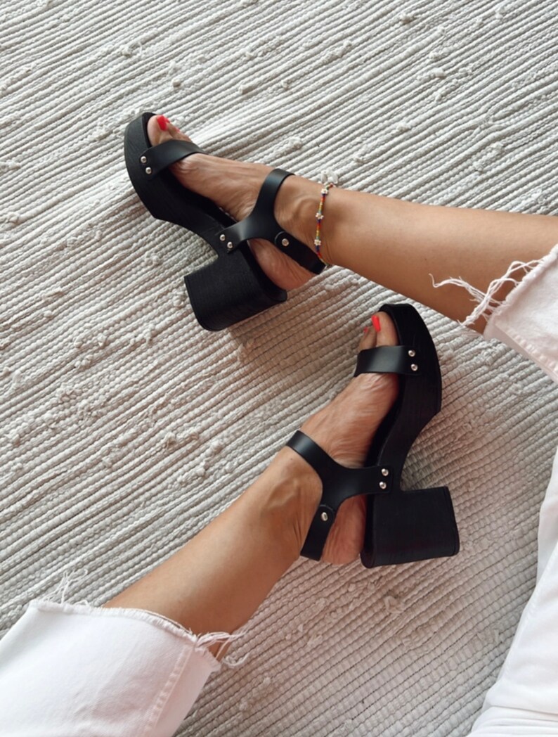 May include: Black platform sandals with a chunky heel and silver studs. The sandals have a strap across the toe and an ankle strap.