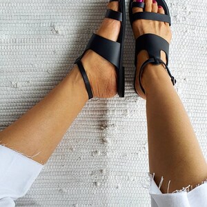 Puede incluir: Un par de sandalias de cuero negro con correas de tobillo. Las sandalias tienen un dise&ntilde;o sencillo con m&uacute;ltiples correas a trav&eacute;s del pie.