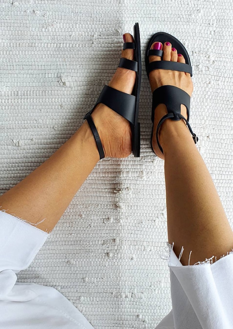 Puede incluir: Un par de sandalias de cuero negro con correas de tobillo. Las sandalias tienen un dise&ntilde;o sencillo con m&uacute;ltiples correas a trav&eacute;s del pie.