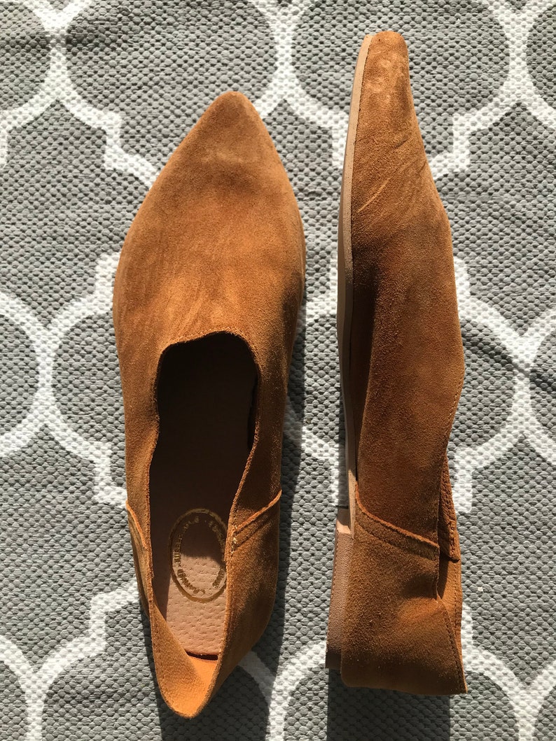 May include: A pair of brown suede slip-on shoes with pointed toes. The shoes have a simple design and are made of soft, comfortable material.