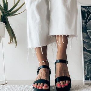 May include: Black platform sandals with ankle straps. The sandals have a chunky heel and are made of leather.