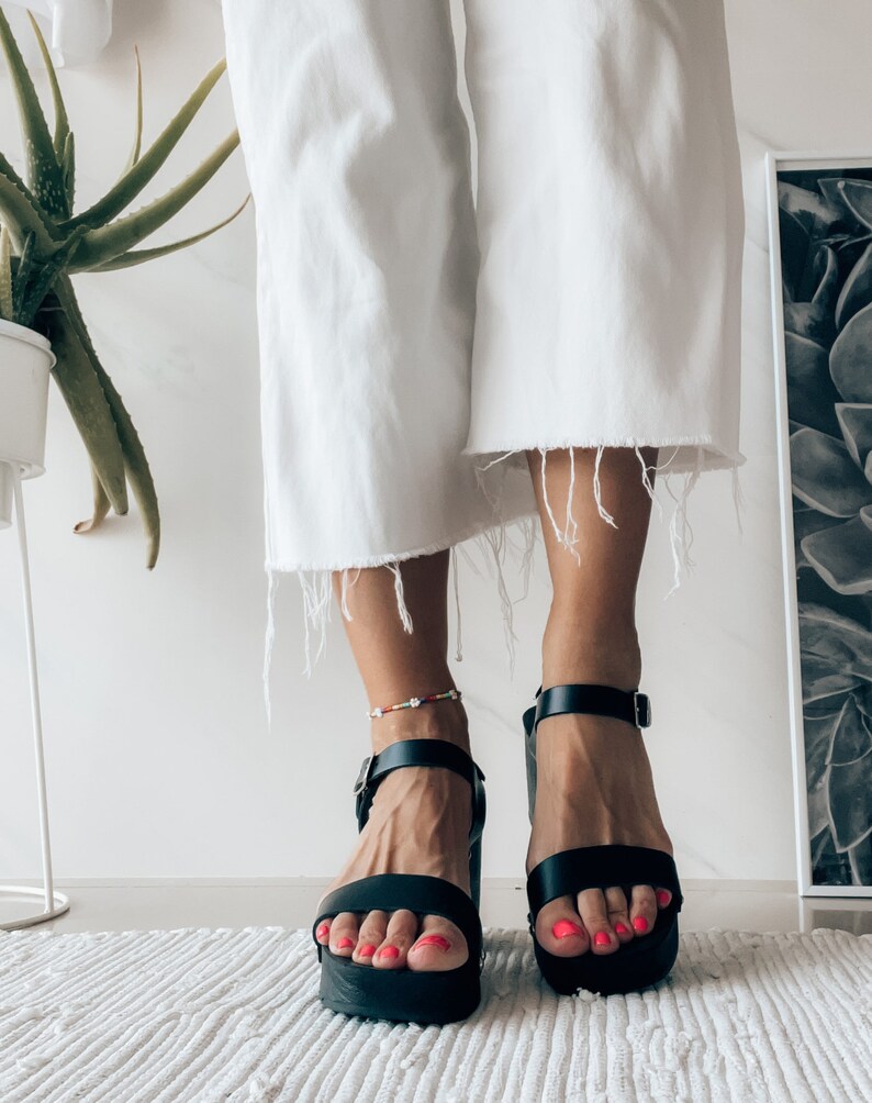 May include: Black platform sandals with ankle straps. The sandals have a chunky heel and are made of leather.