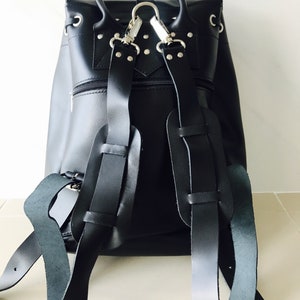 May include: Black leather backpack with silver hardware and adjustable straps. The backpack has a flap closure and a zippered pocket on the front.
