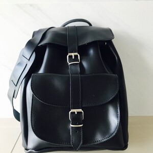 May include: A black leather backpack with two adjustable buckles and a large front pocket.