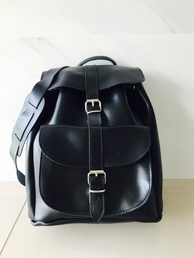 May include: A black leather backpack with two adjustable buckles and a large front pocket.