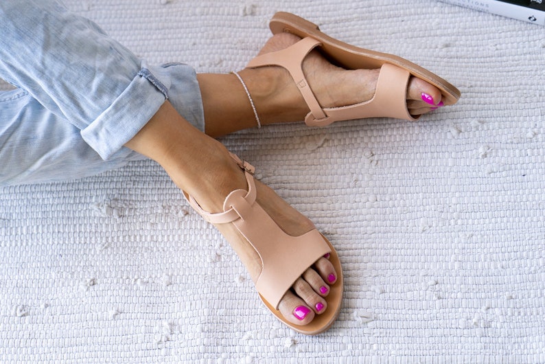 May include: A pair of light brown leather sandals with a t-strap design. The sandals have a simple, minimalist style and are perfect for warm weather.