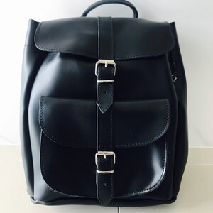 May include: A black leather backpack with two silver buckles and a flap closure. The backpack has a large pocket on the front.