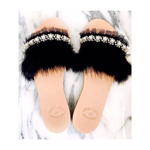 Pu&ograve; includere: Un paio di sandali neri con bordi in pelliccia e un ornamento di perle e tulle. I sandali hanno una suola in pelle e sono contrassegnati con "38" e "Made in Italy".