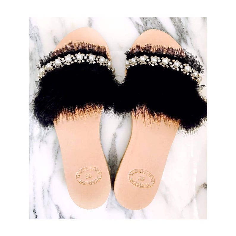 Pu&ograve; includere: Un paio di sandali neri con bordi in pelliccia e un ornamento di perle e tulle. I sandali hanno una suola in pelle e sono contrassegnati con "38" e "Made in Italy".