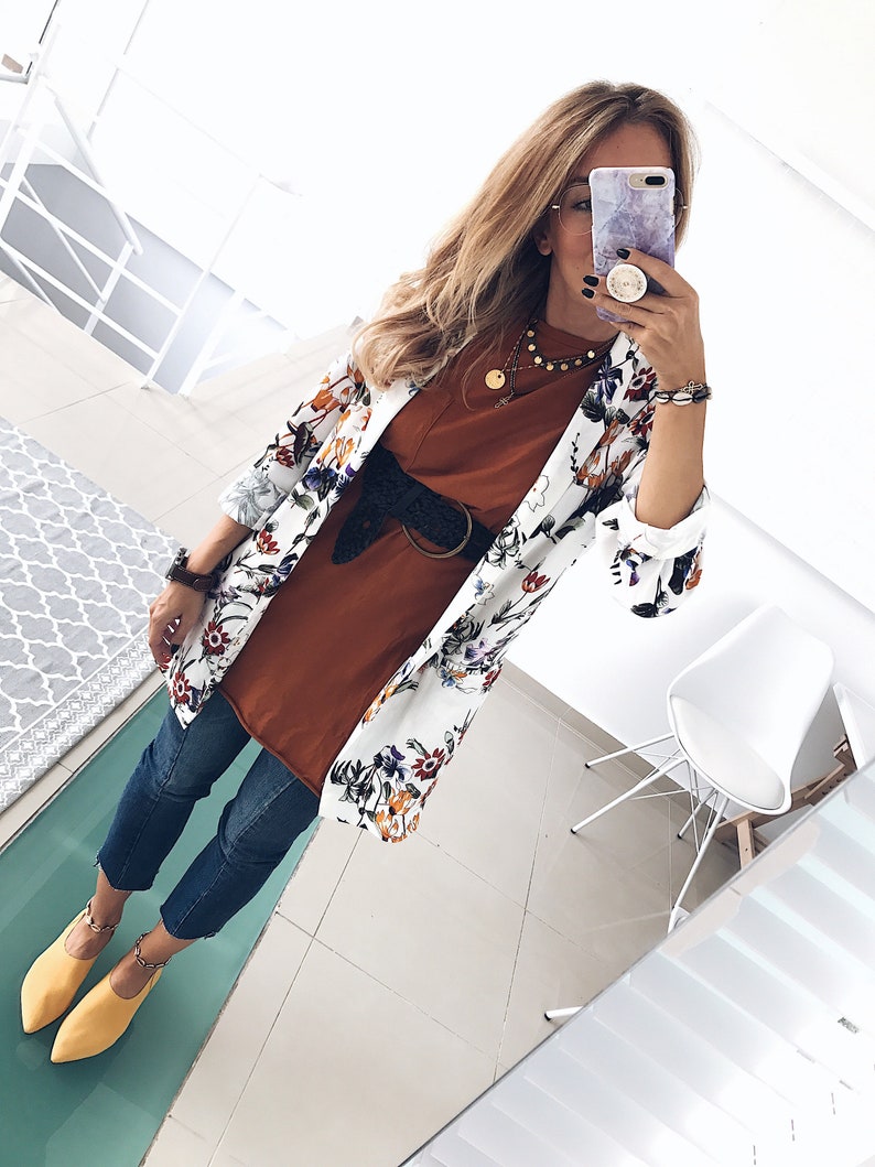 May include: A white floral print blazer with a brown t-shirt, blue jeans, and yellow shoes. The person is wearing a gold necklace and a black belt with a silver buckle.