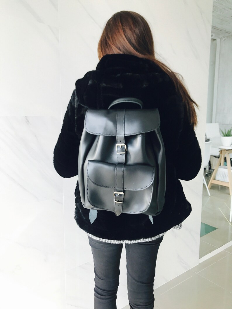 May include: A black leather backpack with two adjustable buckles and a flap closure. The backpack has a single pocket on the front.