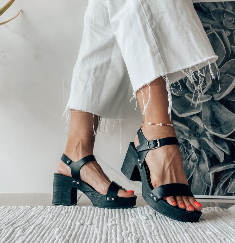 May include: A pair of black leather platform sandals with ankle straps. The sandals have a chunky heel and a thick platform sole.