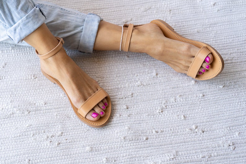 May include: A pair of tan leather sandals with ankle straps. The sandals have a simple design and are perfect for summer.