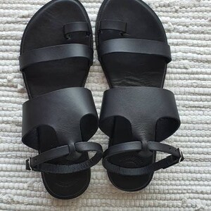 Puede incluir: Un par de sandalias de cuero negro con dos correas y un bucle para el dedo del pie. Las sandalias tienen un dise&ntilde;o sencillo y son perfectas para el clima c&aacute;lido.