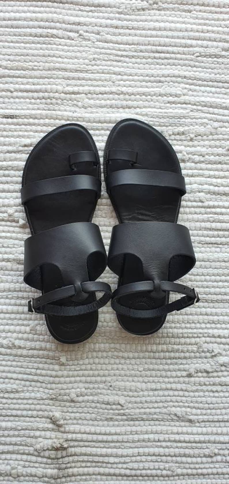 Puede incluir: Un par de sandalias de cuero negro con dos correas y un bucle para el dedo del pie. Las sandalias tienen un dise&ntilde;o sencillo y son perfectas para el clima c&aacute;lido.