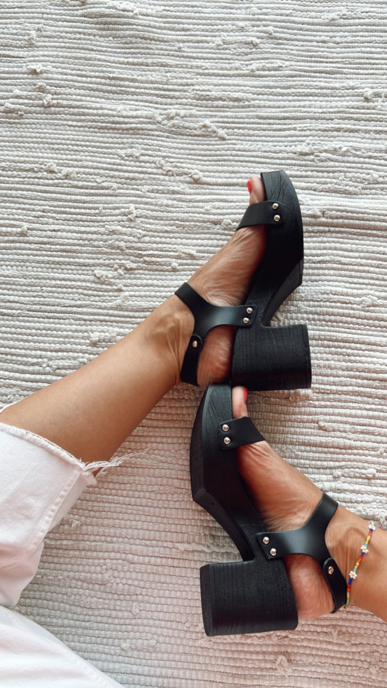 May include: Black platform sandals with silver studs and a thick wooden heel. The sandals have a strap across the foot and an ankle strap.