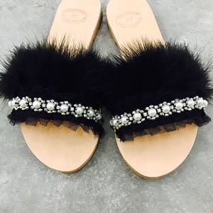 Pu&ograve; includere: Un paio di sandali in pelle nera con bordino in piume nere e un ricamo in tulle nero e perle.