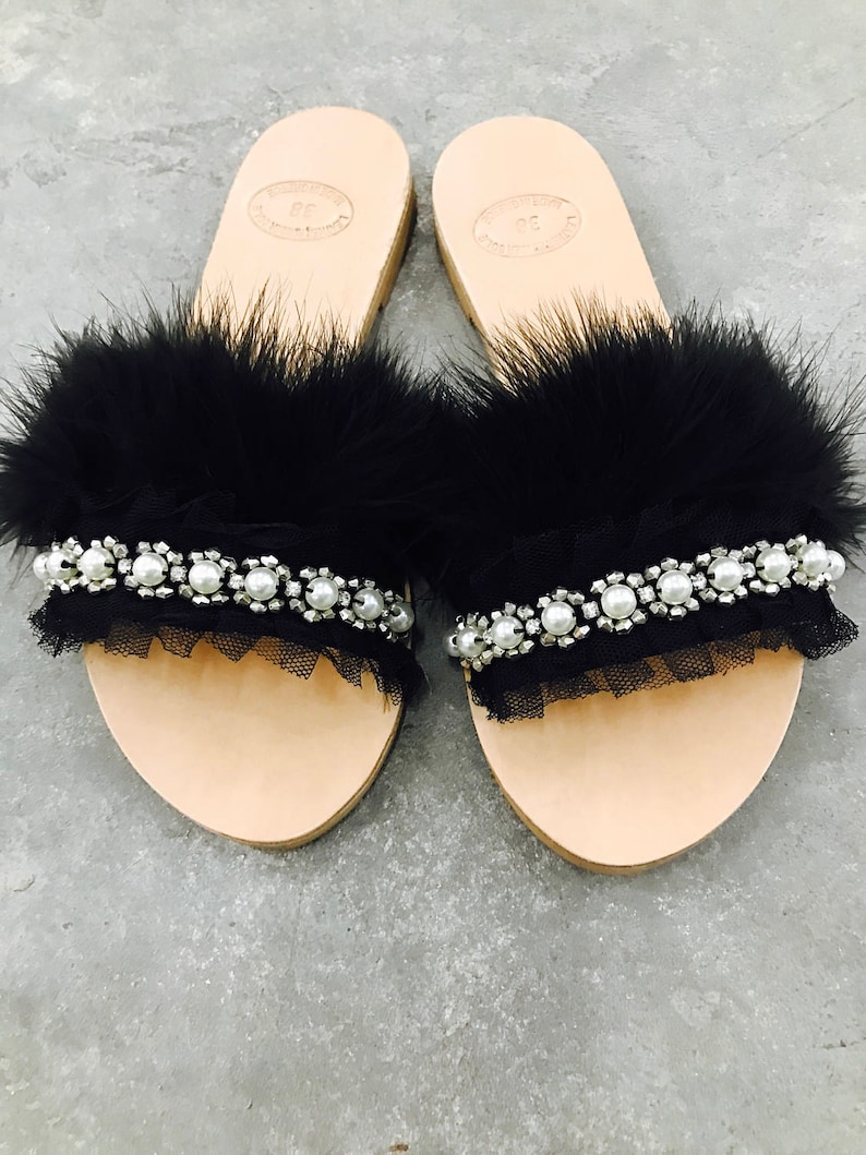 Pu&ograve; includere: Un paio di sandali in pelle nera con bordino in piume nere e un ricamo in tulle nero e perle.