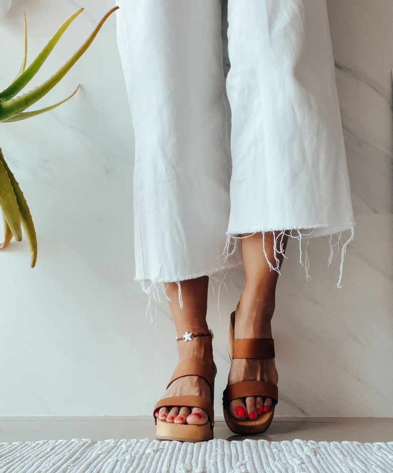 May include: Brown leather platform sandals with a white star ankle bracelet. The sandals have two straps across the foot and a thick platform sole.
