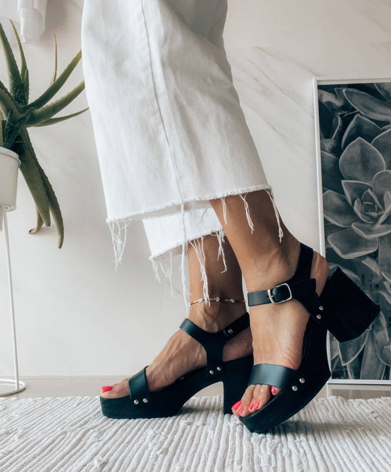 May include: Black leather platform sandals with a buckle closure and a chunky heel. The sandals have a platform sole and are worn on a person's feet.