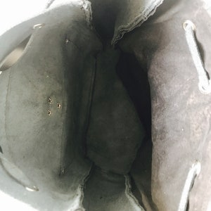 May include: Black drawstring bag with a suede-like texture and a single zipper pocket on the inside. The bag is empty and the drawstring is loose.