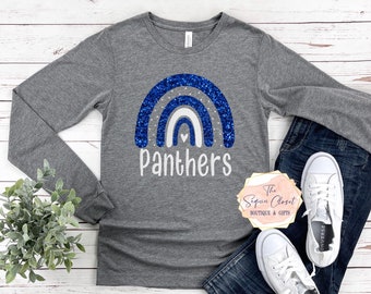 May include: A gray long-sleeve shirt with a blue glitter rainbow and the word "Panthers" in white. The shirt is laid flat on a white wooden surface with a pair of white sneakers and blue jeans.