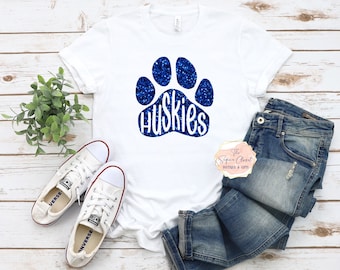 May include: White t-shirt with a blue glitter paw print and the word "Huskies" inside the print.